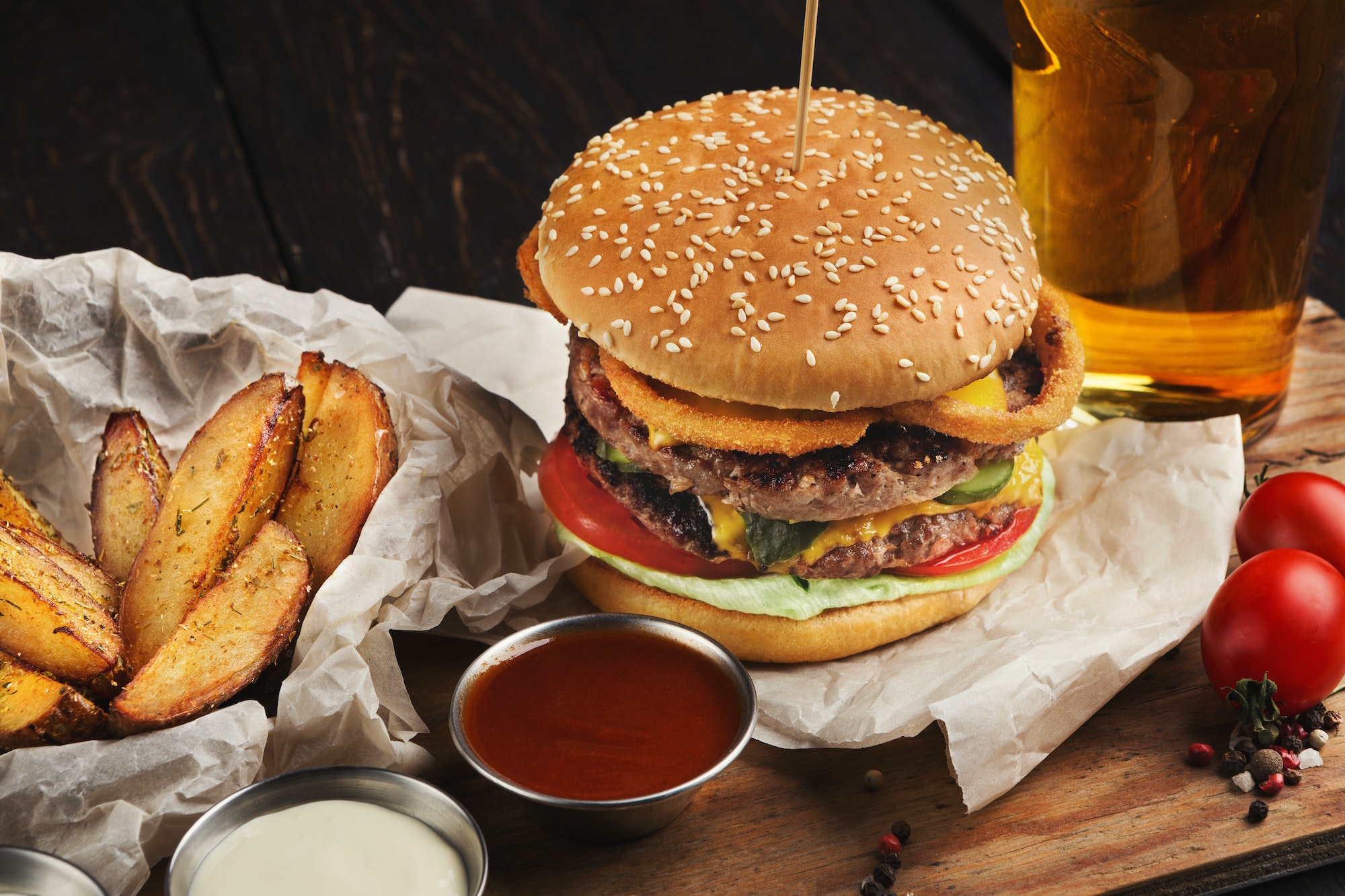 Burger and potatoes served with beer at restaurant, closeup
